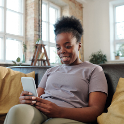 African-American woman sitting on a couch looking at a phone.